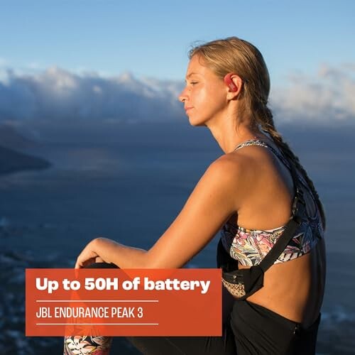 Woman wearing headphones sitting on mountain ledge with sea view